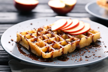 Delicious waffle with apple slices, syrup and chocolate shavings on plate, close up