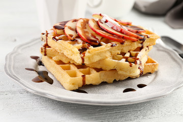 Delicious waffles with apple slices, syrup and sugar powder on plate