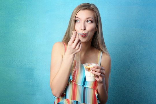 Beautiful young woman eating ice cream on color background