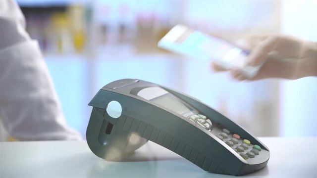 Woman paying through smartphone using NFC technology. Close up.