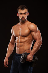 Fototapeta na wymiar Handsome power athletic man with dumbbell is confidently looking forward. Strong bodybuilder with six pack, perfect abs, shoulders, biceps, triceps and chest Isolated on black background with