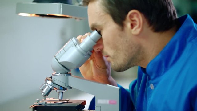 Male researcher working with microscope. Close up of lab researcher looking in microscope. Medical researcher doing microscope research. Research medical microscope