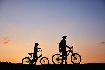 Fototapeta na wymiar Biker family silhouette, father with kid on bikes at sunset