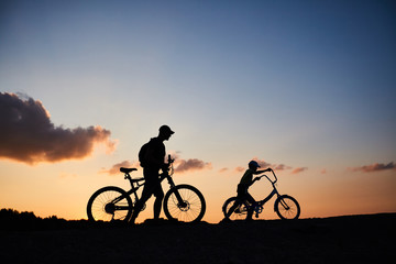 Obraz na płótnie Canvas Biker family silhouette, father with kid on bikes at sunset