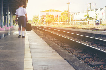 Fototapeta premium Asian boy waiting train at train station.Back of child with sunset.