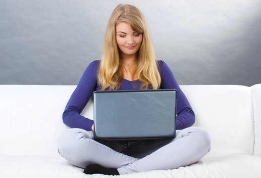 Happy woman using laptop sitting on sofa, modern technology