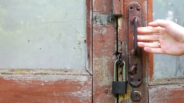 A human hand takes the door handle of a red brown rotten door