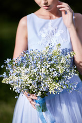 blue bouquet in hands of the girl in a blue dress.  Lilies of the valley and forget-me-nots