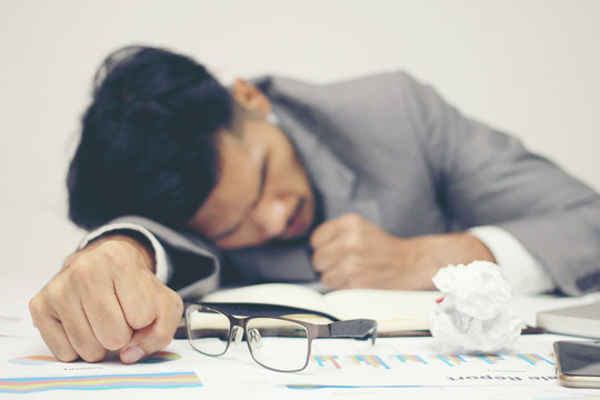 Businessman sleeping at his desk working over a laptop on background after he work all day all night, Tried overworked, Keep fighting in business concept.