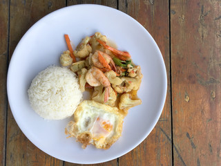stir-fry vegetables with bean curd and shrimp in white dish with rice and fried egg on wooden background. Thai style Food.