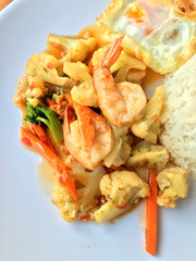 stir-fry vegetables with bean curd and shrimp in white dish with rice and fried egg on wooden background. Thai style Food.
