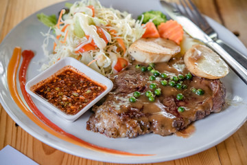 Beef steaks with grilled vegetables and seasoning on wooden background