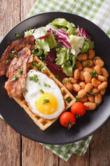 hearty breakfast with fried egg, waffles, bacon, mix salad and beans close-up. Vertical top view