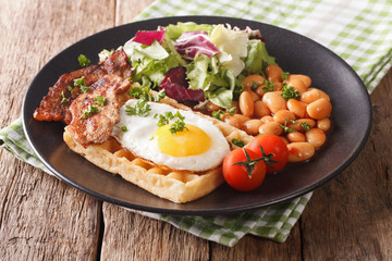 hearty breakfast with fried egg, waffles, bacon, mix salad and beans close-up. horizontal