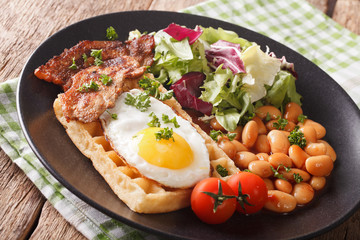Breakfast with fried egg, waffles, bacon, mix lettuce and beans close-up. horizontal