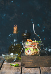 Homemade jar quinoa salad with sun-dried tomatoes, avocado and fresh basil leaves. Detox, dieting, vegetarian, vegan, clean eating food concept. Dark blue background, selective focus, copy space