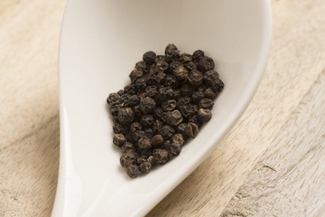 black pepper in white spoon on wooden background