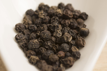 black pepper in white spoon on wooden background