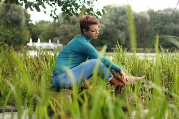 Naklejka na ściany i meble Beautiful emotional girl sits on a lake among the grass and water
