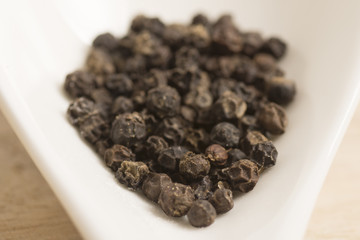 black pepper in white spoon on wooden background