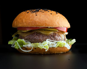 Burger, white bun with one cutlet, cheese, salad and pickled onion on a black background