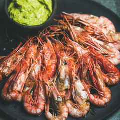Roasted red shrimps with guacamole avocado sauce in slate stone black plate over grey concrete background, selective focus, square crop