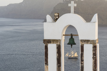 Traditional church belfry and sailing boat at sunset in Oia, Santorini, Greece © respiro888