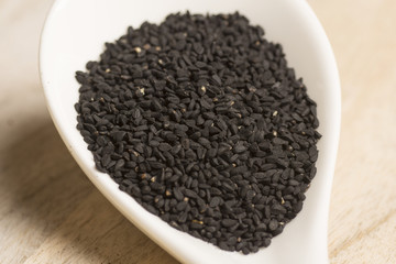 black seeds in white spoon on wooden background