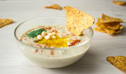 A bowl of creamy hummus with olive oil and chips.