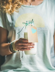 Young blond woman in light t-shirt holding bottle of dairy-free almond milk in her hand. Clean...