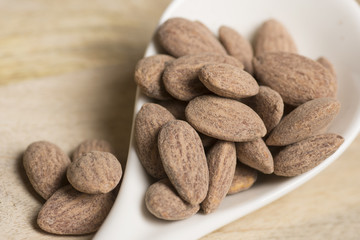 closeup of salt almonds nut in white spoon wooden background