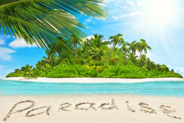 Whole tropical island within atoll in tropical Ocean and inscription "Paradise" in the sand on a tropical island.