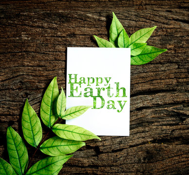 Happy Earth Day paper sheet with fresh spring  green leafs border frame on wooden background , eco natural banner concept