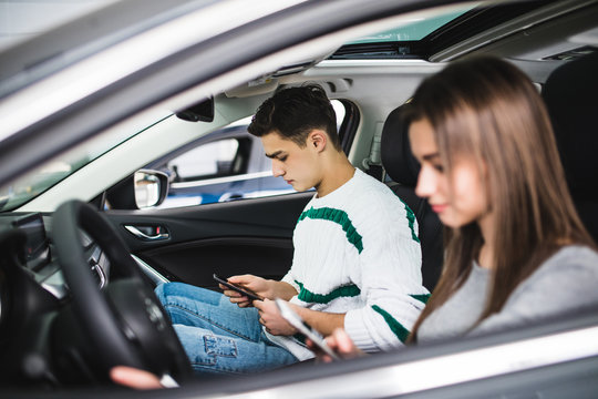 Portrait of a young couple use phones, texting and driving together, as seen through the windshield