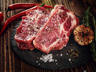 Raw pork neck steak on a stone plate.