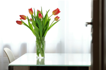 Red tulips in a glass vase on a glass table