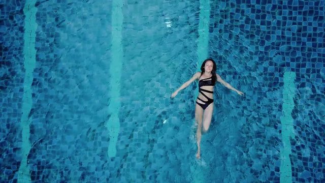 Top view aerial photo of a seductive sexy model in black swimwear is enjoying relax in hotel pool. Amazing fashion woman in bikini having luxury spa rest