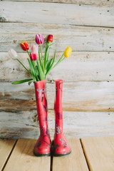 colorful rain boots with spring flowers  in wooden background.