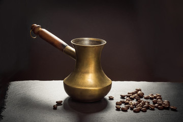 Black coffee in old copper cezve and coffee beans on black slate as background with copy space.