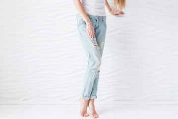 Women’s legs in blue jeans with white pedicure on a white background. White manicure