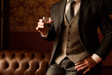 Groom holds in his hand a glass of whiskey indoors. Stylish man's hand with a ring on the little...