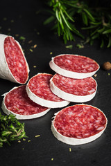 Salami sausage sliced with rosemary, olives and spices on the dark background. Shallow depth of field.