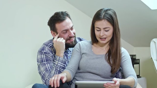 Beautiful Couple using a digital tablet sitting on a bed at home