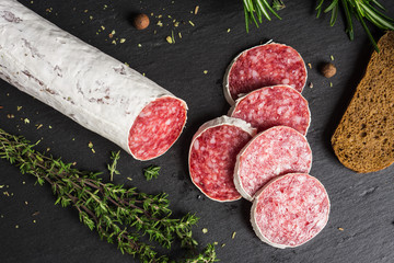 Salami sausage sliced with rosemary, olives and spices on the dark background