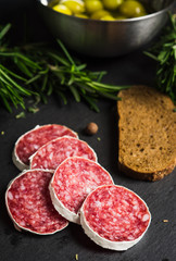 Salami sausage sliced with rosemary, olives and spices on the dark background. Shallow depth of field.