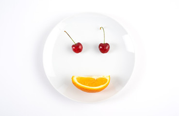 Healthy smile face created of two cherries and orange on the white plate isolated on white background