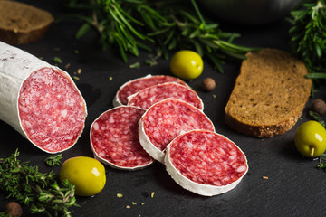 Salami sausage sliced with rosemary, olives and spices on the dark background. Shallow depth of field.