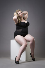 Young beautiful blonde plus size model in shapewear, xxl woman in slimming underwear on gray studio...