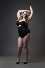 Young beautiful blonde plus size model in shapewear, xxl woman in slimming underwear on gray studio background