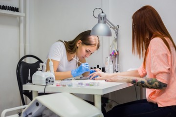 Manicurist treating client at beauty salon. Manicure stage: Painting on the nail